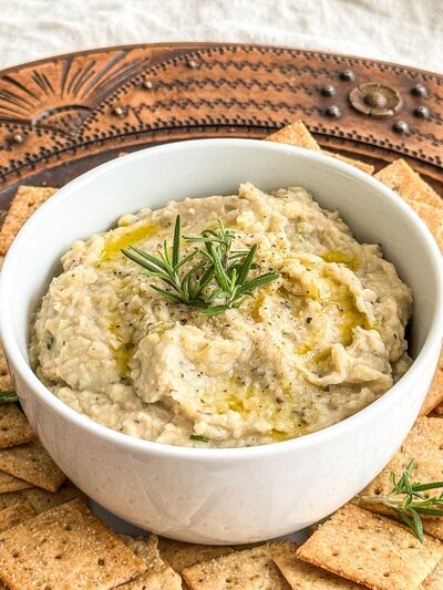A  bowl of white bean dip topped with olive oil, fresh rosemary and black pepper.