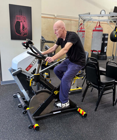 A Parkinson's warrior rides a workout bike in the Warriors Gym, representing the diversity of the Parkinson's exercise classes offerings. 