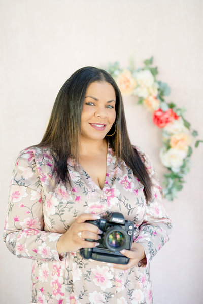 Photographer Kiamarie Stone smiles for photo holding camera in floral dress