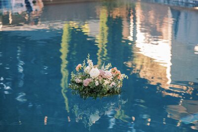 A floral centerpiece afloat in a pool at a wedding with flowers designed by Flowers and Thyme.