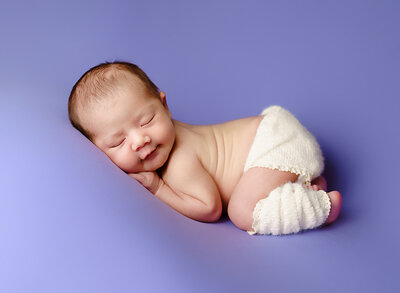 A tiny little newborn boy yawns during his newborn photography session.