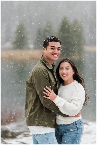 a man and woman stand close together while smiling at the camera with snow falling around them