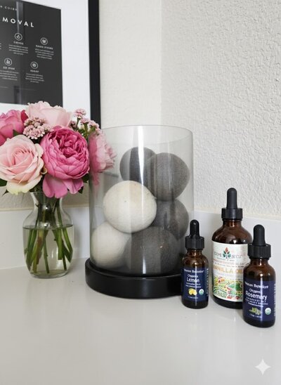 wool laundry balls in glass container next to essential oils and pink flowers non-toxic laundry solutions for hormonal balancing