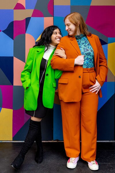 A person leaning up against their partner in front of a colorful wall.