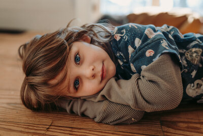 Little boy lays down on floor and looks into camera with big blue eyes