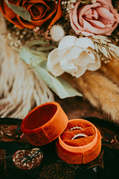 wedding rings in ring box in front of flowers with autumn tones