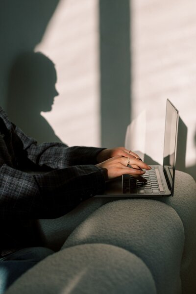Woman sitting on couch typing on laptop - Refined Web Design