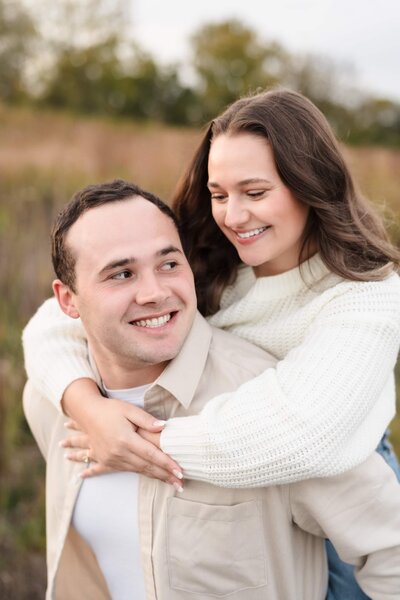 A young woman in a white sweater hugs onto her fiance and smiles at him