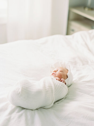 photo of newborn baby swaddled on bed by madison wi family photographer talia laird photography