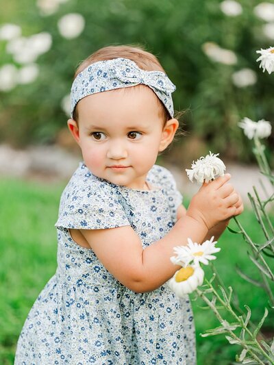 Little Girl with a blue dress holding a white flower outside.
