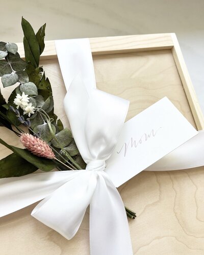 White gift tag with calligraphy on wood box with white satin ribbon and dried flowers