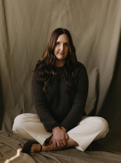 Portrait of the Gatherie Creative founder seated cross-legged against a draped olive backdrop, conveying her approachable brand design expertise.