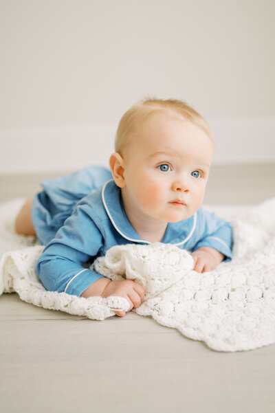 Baby boy with blue collared outfit lays on knit blanket during baby studio photography session