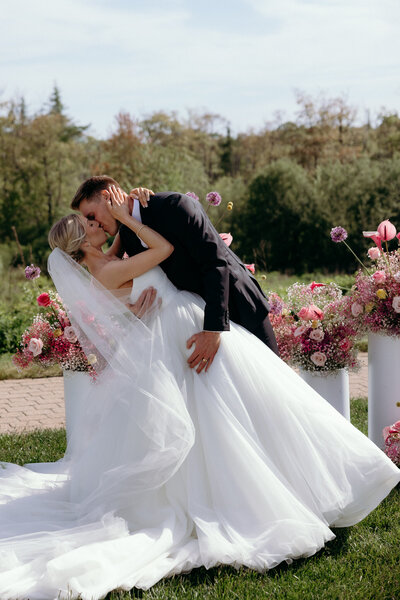 VT Wedding Photographer | Sincerely Liz Photography Documentary Wedding, Engagement, Elopement, Maternity and Newborn Photographer in New England | Bride and groom kiss in front of pink floral arrangements