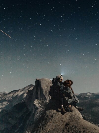 a couple sitting on a rock at night in the mountains under the stars
