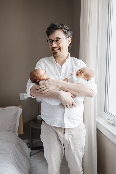 new dad holding his twin daughters captured by Toronto Newborn Photographer Claire Binks