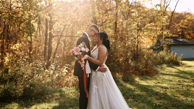 couple in front of fall colored trees with the golden hour glow shining through