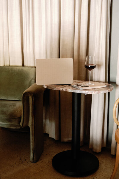 Laptop and wine glass on a marble table next to a green velvet chair