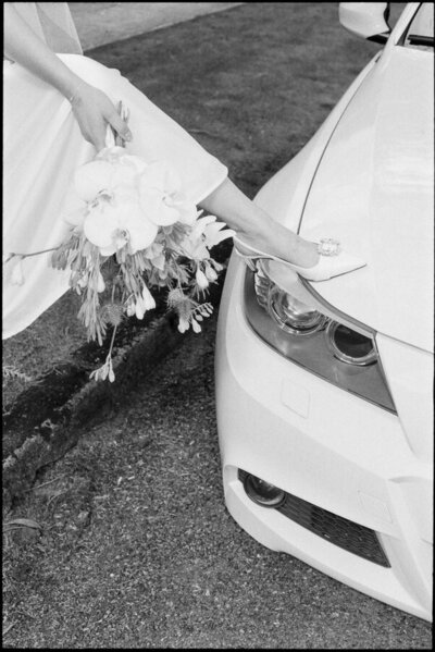 35mm film editorial style photo of bride holding her bouquet with a luxury car