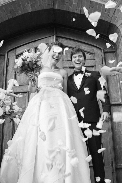 Les mariés sont devant les portes de l'église, après la cérémonie. Les invités lancent des pétales. Photographe de mariage.