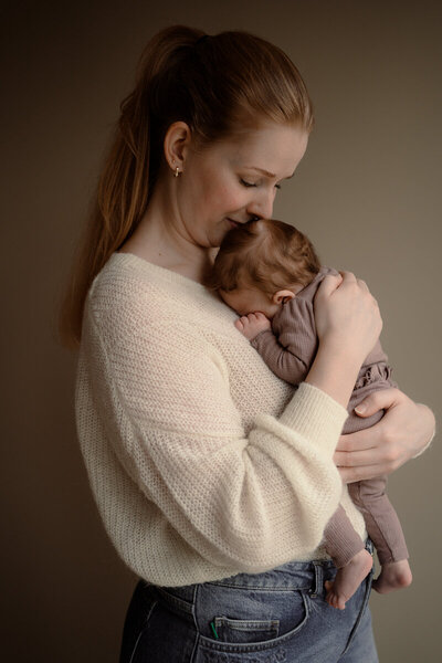 Moeder houdt baby dicht tegen haar borst aan tijdens een newbornshoot en ruikt aan haar haartjes