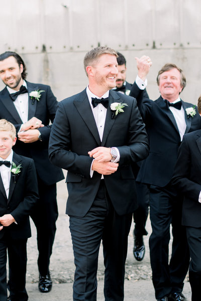 groom and groomsmen in their black tie tux adjusting cufflinks while walking towards the camera at the foundry at puritan mill by atlanta wedding photographer lane albers photography