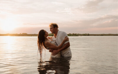 A couple standing in a lake with the water waist high. They are holding and looking at each other, smiling.
