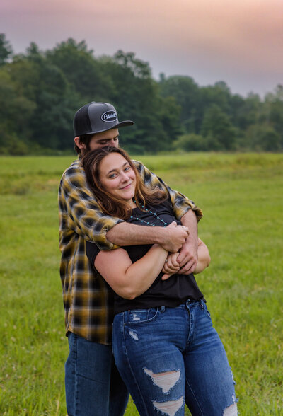 Intimate portrait of young couple, sitting against a tree in the woods.