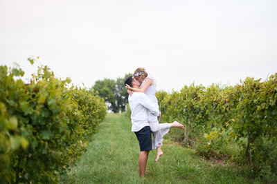 Girl in purple vintage dress and flower crown kissing her fiance in a vineyard
