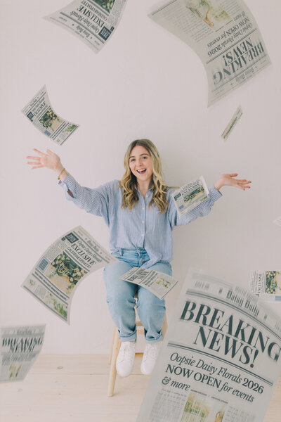 Woman tossing styled floral newspapers in a minimal white studio, smiling and celebrating the launch of 2026 floral calendar. Greenville South Carolina portrait photographer – Dani Lacey Photographs.