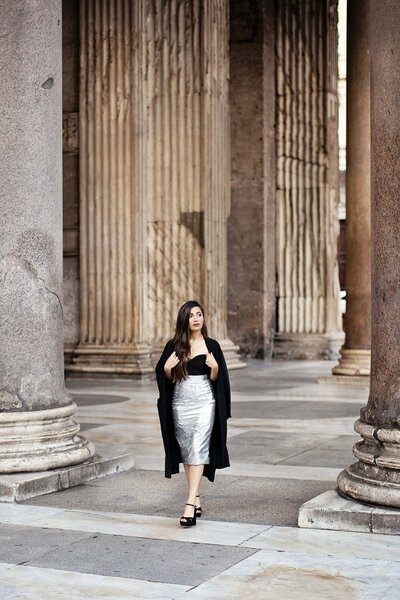 A girl walking in between the columns of the Pantheon in a silver skirt and black top and cape. Taken by Rome Vacation Photographer, Tricia Anne Photography.
