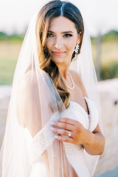 Close up image of a bride smiling at the camera with her veil partially covering her face