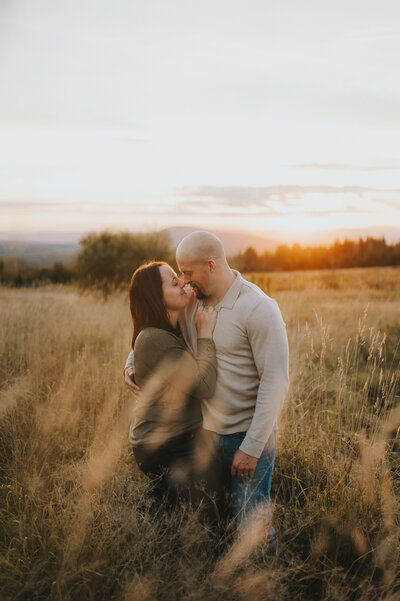 Kelsey and her husband facing each other in a field with the sunset in the background.