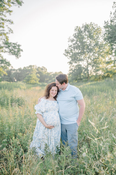Husband and wife standing together in a field, embracing the anticipation of welcoming their new baby, surrounded by nature in a peaceful moment