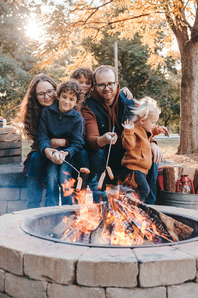 Family of five - mom, dad, two boys and a little girl. sitting at fire pit, roating hot dogs.  little girl is jumping off of dad's lab - see you later I am out of here ...  Family Portraits - Campfire sessions