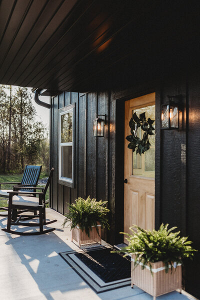 Front porch of all black exterior photography studio with ferns and two rocking chairs