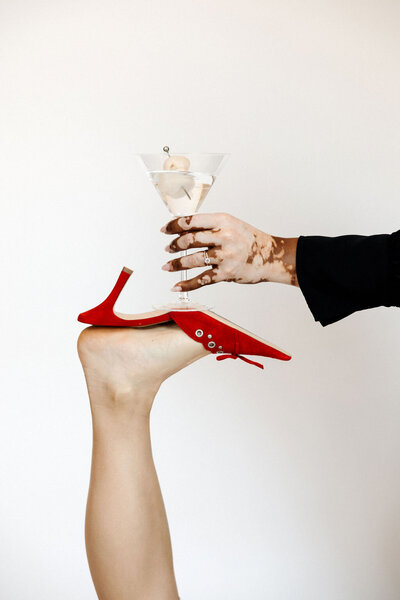 A martini glass with a rose-hued beverage on a modern black table with a Dior magazine