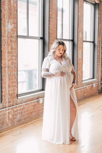 Pregnant woman in white dress looks at her belly