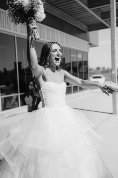 Bride dances and celebrates after walking down the aisle. She is wearing a corset wedding gown with a strapless, sweetheart neckline. Photographed by Anna Brace, who specializes in Omaha Wedding Photography.