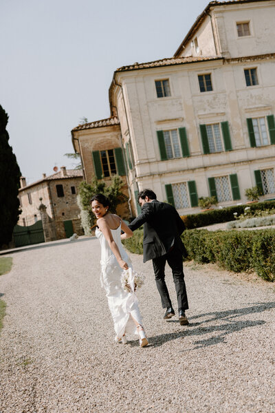 A newlywed couple holding hands and walking along a gravel road 