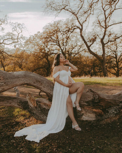 pregnant woman posing on log in white dress