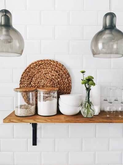 “Minimalist kitchen shelf styled with glass jars of grains and flour, stacked white bowls, and a woven placemat, representing simple, whole-food living.