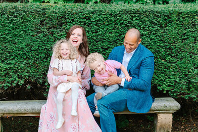 Playful family of four — mother, father, and two children — laughing together during a Paris family photoshoot at Place des Vosges in the Marais.