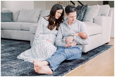A newborn session where mother and father sit in front of their couch, holding their infant son, photographed by Newborn Photographer Maryland Marie Elizabeth Photography