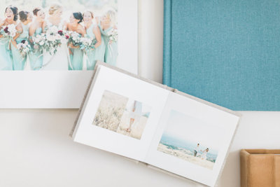 White background with linen photo album lying open and teal photo album placed underneath it