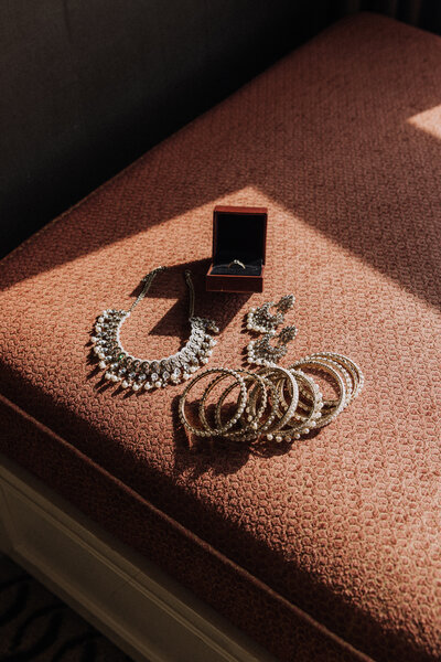Luxury South Asian bridal jewelry flatlay with gold bangles, pearl necklace, earrings, and engagement ring captured in natural window light for wedding detail photography.
