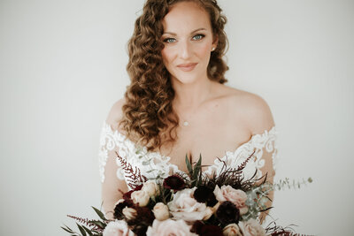 Bride standing in ballroom holding bouquet down at her side in one hand looking away from the camera out the window