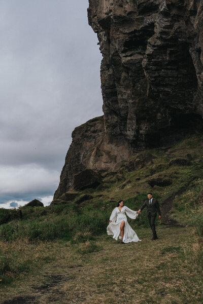 Husband and wife walk hand in hand down a grassy hill in Iceland