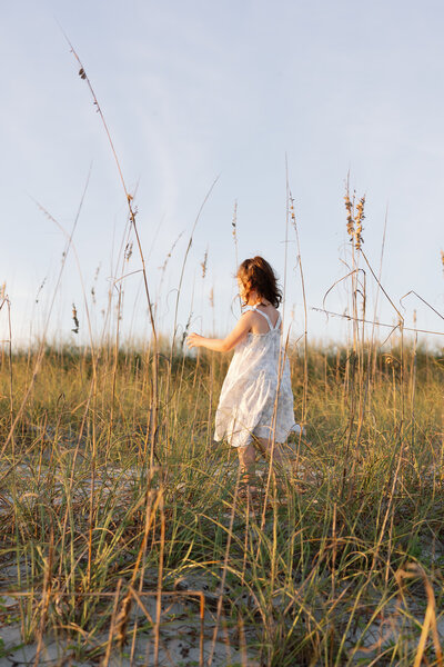 Golden-hour family portrait in a green field; a little girl runs through the wheat field