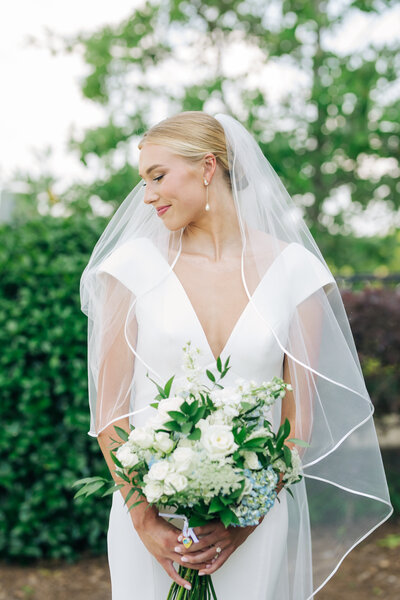 Bride wearing a veil and holding a bouquet of flowers on a summer day in Mississippi